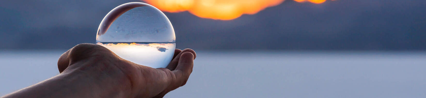 Une main tient un globe de verre devant un coucher de soleil