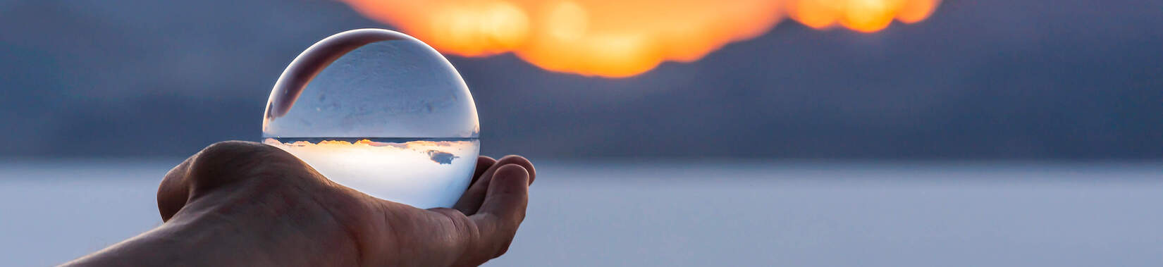 Een hand houdt een glazen bol vast voor een zonsondergang