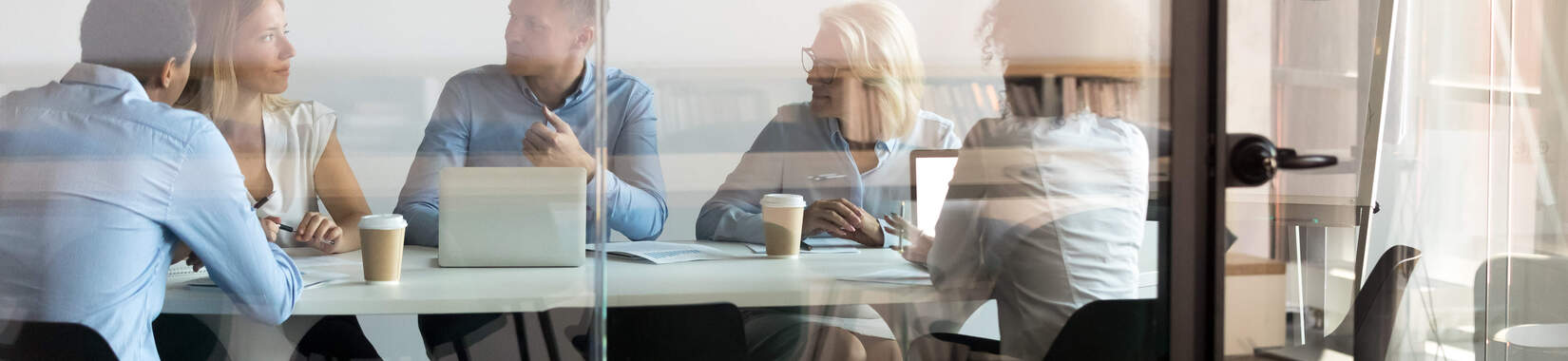 A team has a meeting in a conference room behind a glass door